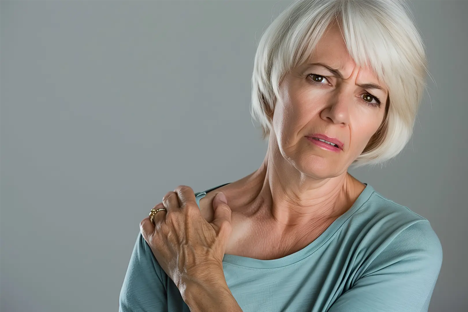 A woman with a pained expression, clutching her shoulder, experiencing significant shoulder pain