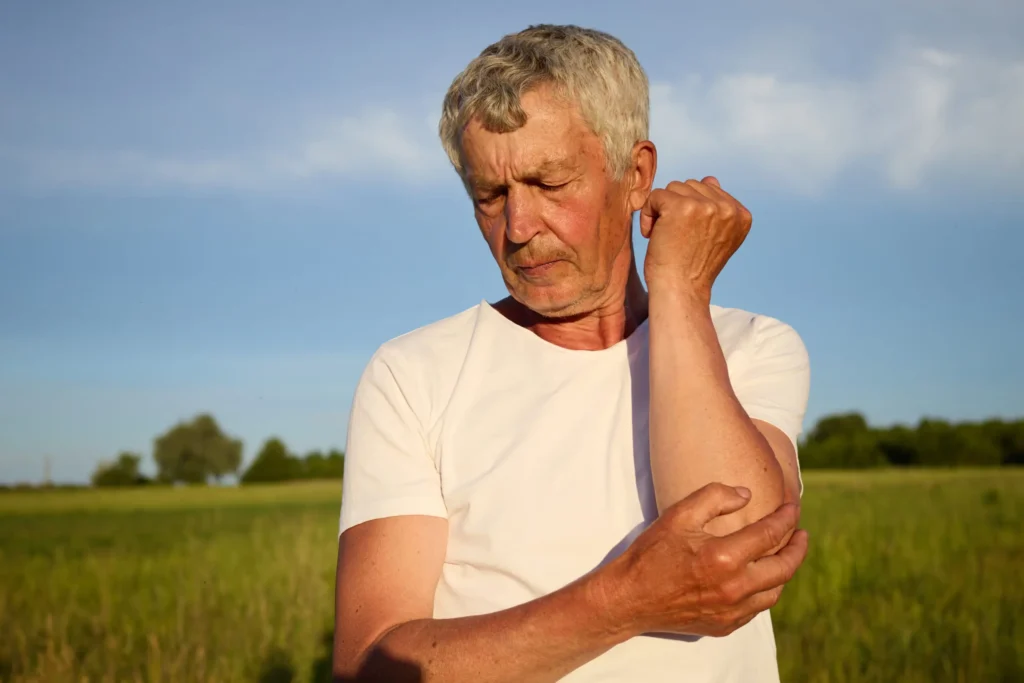 Golfer’s elbow pain: older man pressing inner elbow outdoors