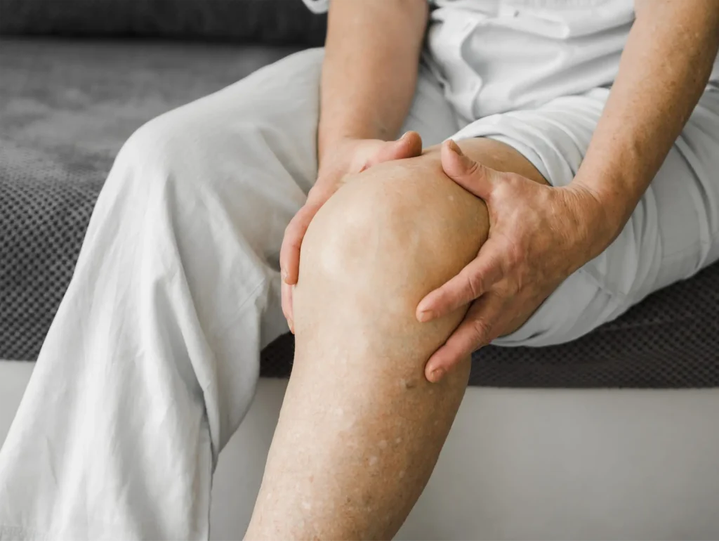Elderly person holding painful knee joint due to arthritis, sitting on bed