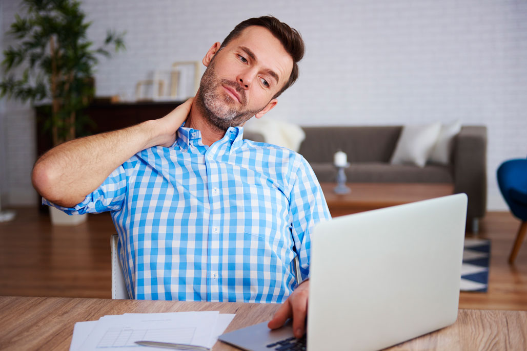 Office worker with neck strain rubbing sore neck at computer desk