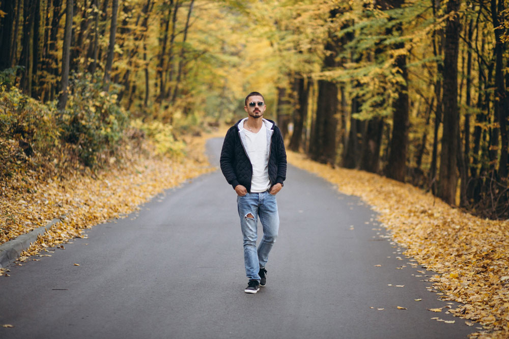 Young man walking on a road in an autumn park